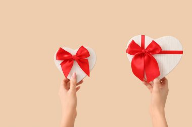 Bej arka planda kalp şeklinde hediye kutuları olan kadın elleri. Sevgililer Günü kutlaması