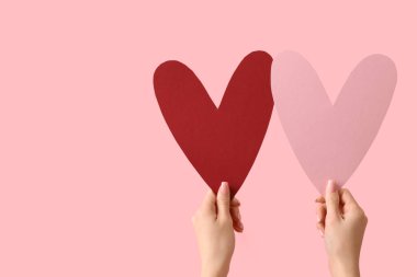 Pembe arka planda kağıt kalpli kadın eller. Sevgililer Günü kutlaması