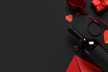 İçinde hediye kutusu olan bir şişe şarap, kağıt kalpler, hava balonu ve siyah arka planda bir zarf. Sevgililer Günü kutlaması