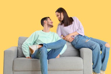 Güzel, genç ve mutlu bir çift, sarı arka planda, kanepede birlikte vakit geçiriyorlar.