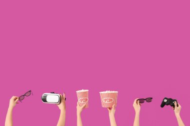 Patlamış mısır, VR kulaklık, 3 boyutlu gözlük ve pembe arka planda oyun pedi olan eller.