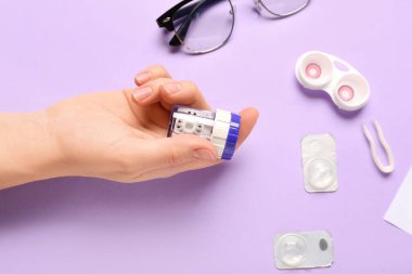 Lens, gözlük ve leylak arkaplan üzerine konteyner için temizlik çantası olan kadın elleri