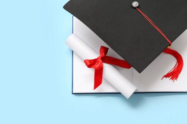 Diplomalı mezuniyet şapkası ve mavi arka planda not defteri.