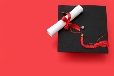 Kırmızı arka planda mezuniyet şapkası ve diploması.