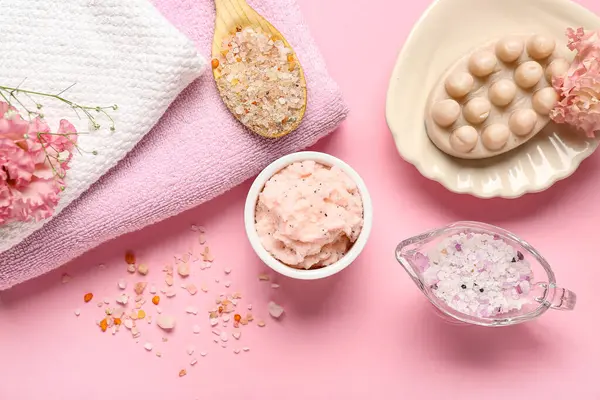 Pembe arka planda vücut fırçası, deniz tuzu ve temiz havlular.