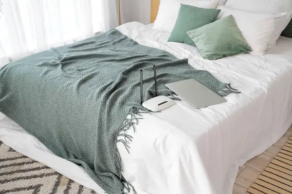 Yatakta dizüstü bilgisayarı olan modern wi-fi yönlendirici.