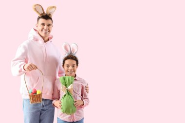 Pembe arka planda Paskalya yumurtaları olan tavşan kulaklı küçük çocuk ve babası