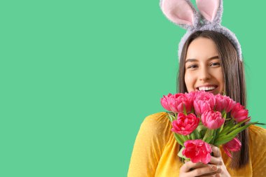 Yeşil arka planda laleleri olan tavşan kulaklı genç bir kadın, yakın plan. Paskalya kutlaması
