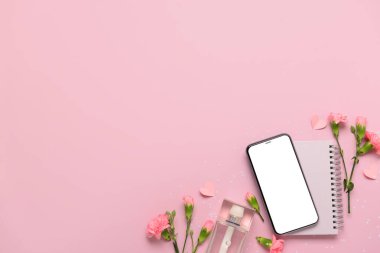 Modern cep telefonlu kompozisyon, bir şişe parfüm ve pembe arka planda karanfil çiçekleri.