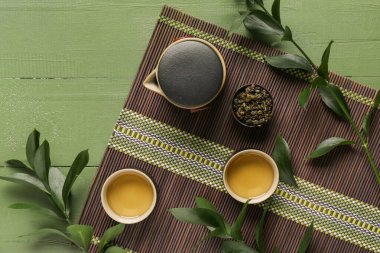 Bambu hasırı, fincanlar dolusu lezzetli çay, çaydanlık ve yeşil yapraklı kase.