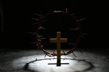 Ahşap haçlı dikenli taç ve siyah grunge arka planda ışık.