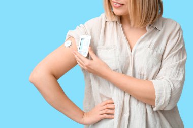 Mavi arka planda kan şekerini ölçmek için glukometresi ve sensörü olan bir kadın. Diyabet kavramı