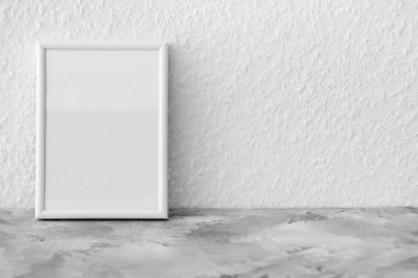 Beyaz duvarın yanındaki gri masada güzel boş fotoğraf çerçevesi.