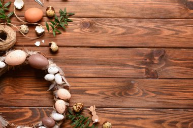 Ahşap arka planda yumurta ve tüylerle süslenmiş Paskalya çelengi.