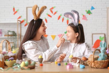 Küçük kız ve annesi tavşan kulaklı. Mutfakta paskalya yumurtası boyuyorlar.