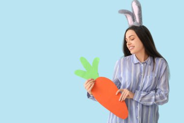 Paskalya tavşanı kulaklı, mavi arka planda kağıt havuç olan güzel, genç bir kadın.