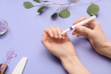 Tırnaklara, okaliptüs dalına ve leylak arkaplana deniz tuzu süren kadın elleri.