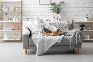 Beyaz bornoz ve oturma odasındaki kanepede farklı banyo malzemeleri.