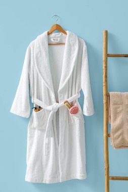 Mavi arka planda farklı banyo malzemeleri asılı beyaz bornoz.