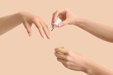 Bej arka planda bir şişe tırnak eti yağı olan kadın elleri.