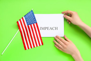 Amerikan bayrağı ve yeşil arka planda IMPEACH pankartı olan kadın eller