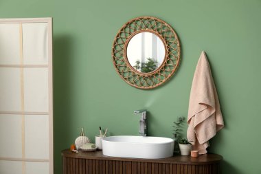 Tezgahta banyo malzemeleri ve banyoda yeşil duvarın yanında şık bir ayna olan modern lavabo.