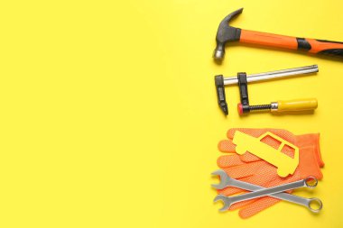 Sarı arka planda bir takım mekanik aletler, eldivenler ve kağıt araba. Mekanik kavram