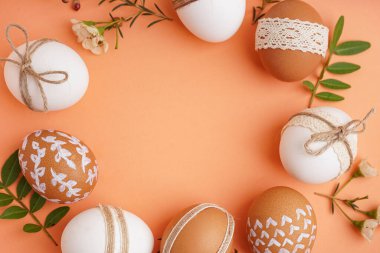 Paskalya yumurtalarından, çiçeklerden ve turuncu arka planda yapraklardan yapılmış güzel bir çelenk.