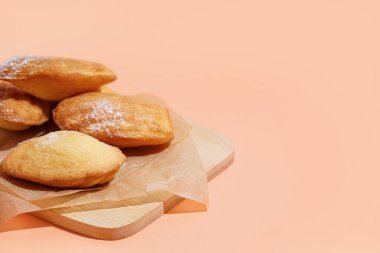 Lezzetli madeleine ve turuncu arka planda pudra şekerli ahşap tahta.
