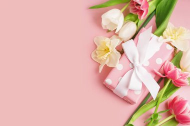 Pembe arka planda güzel laleler ve nergis çiçekleri olan hediye kutusu.