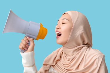 Genç Asyalı Müslüman kadın mavi arka planda megafona bağırıyor. Ulusal Duyulma Günü