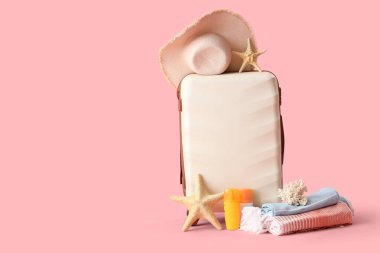 Çanta, plaj aksesuarları, güneş kremi ve pembe arka planda dekor.