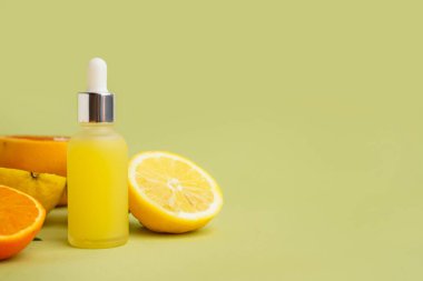 Yeşil arka planda bir şişe temel yağ ve taze narenciye meyvesi.
