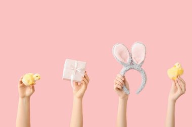 Paskalya tavşanı kulaklı kadın elleri, saç bandı, hediye ve pembe arka planda piliçler.