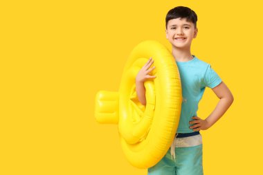 Sarı arka planda şişirilebilir yüzüğü olan sevimli küçük bir çocuk.