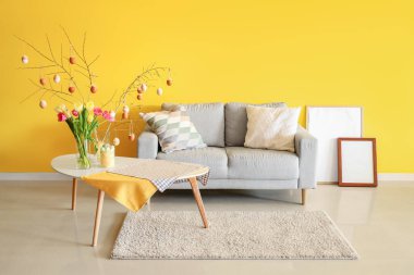 Ağaç dalları olan vazolar, oturma odasındaki masada Paskalya yumurtaları ve laleler.