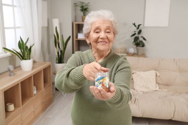 Evde elinde ilaç şişesiyle gülümseyen son sınıf öğrencisi kadın.