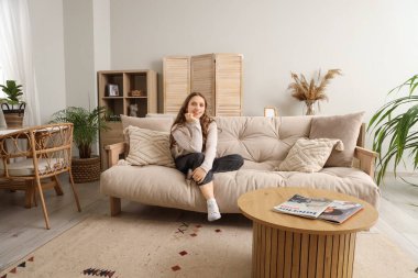 Evdeki yumuşak kanepede oturan genç kadın.