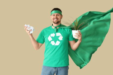 Çevreci süper kahraman gibi giyinmiş genç bir adam. Ev bitkisi ve bej arka planda çöp. Ekoloji kavramı