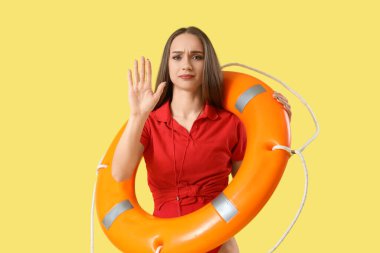 Kurtarma yüzüğüyle genç bayan cankurtaran sarı arka planda DUR hareketi gösteriyor.