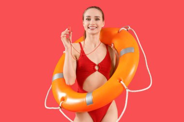 Kurtarma yüzüğüyle ve kırmızı arka planda ıslık çalan genç bayan cankurtaran.