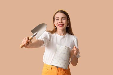 Sulama kabı ve kahverengi arka planda bahçe küreği olan güzel genç bir kadın.