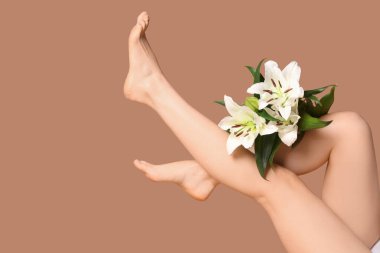 Kahverengi arka planda güzel beyaz zambak çiçekleri olan genç bir kadının bacakları.