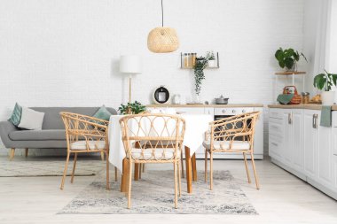 Mutfağın içinde beyaz tezgahlar, gri kanepe ve yemek masası var.