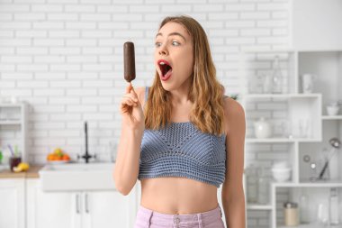 Evde çikolata kaplı dondurma tutan şaşırmış genç bir kadın.