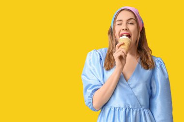 Dondurmayı gözleme kabında ısıran ve sarı arka planda göz kırpan genç bir kadın.