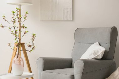 Oturma odasındaki beyaz duvarın yanında çiçek açan vazolardan oluşan gri koltuk ve kahve masası.