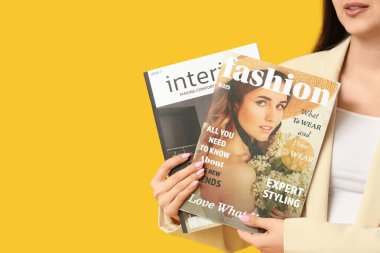 Sarı arka planda dergileri olan güzel bir genç kadın, yakın plan.