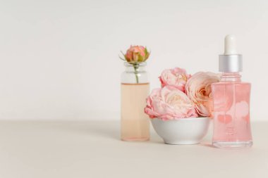 Bej arka planda kozmetik yağı, kase ve güller içeren kompozisyon