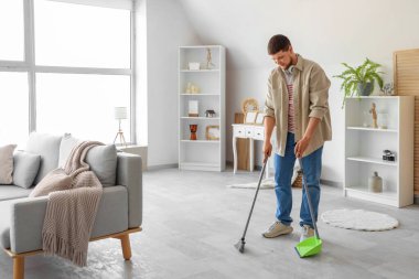 Genç sakallı adam süpürgeyle yerleri süpürüyor.